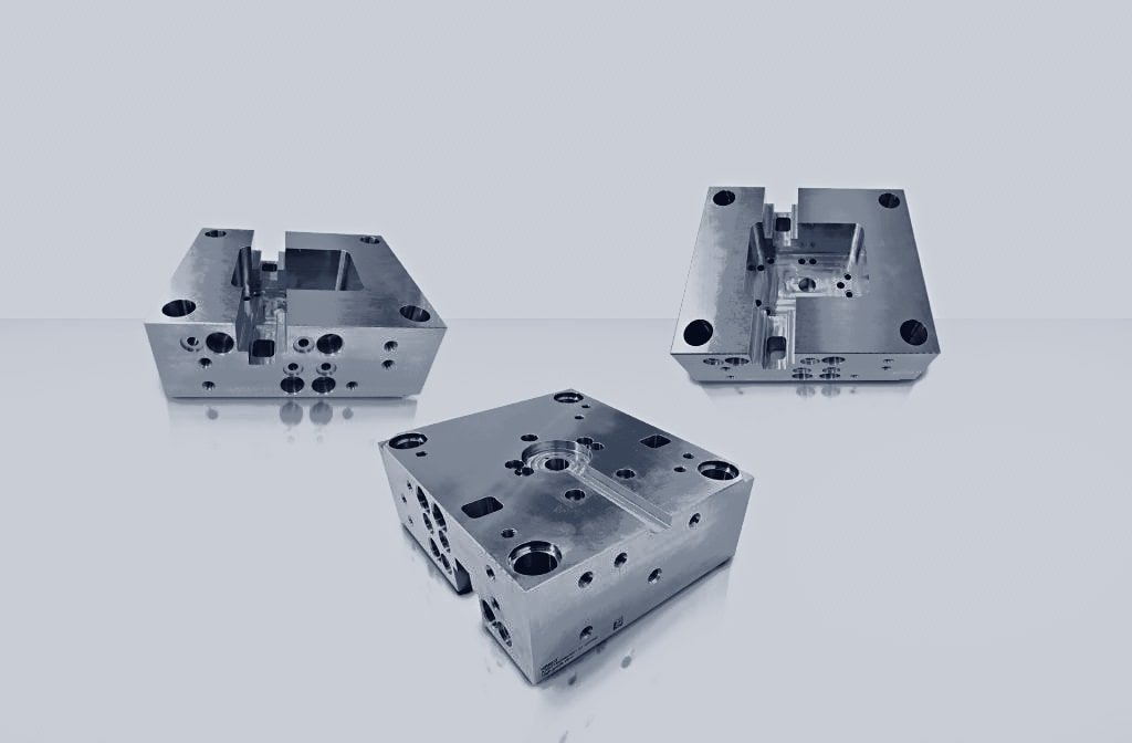 Three CNC-machined mould base plates with cavities, pockets and bolt holes, shown from different angles.